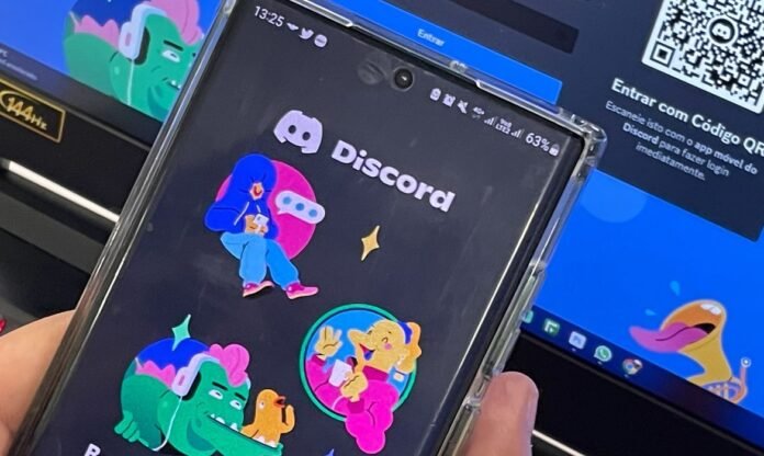 Celular exibe o aplicativo Discord diante de uma tela de computador
